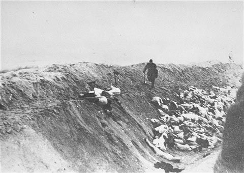 A Latvian policeman walks along the edge of a mass grave towards the bodies of Jewish women and children who have just been executed